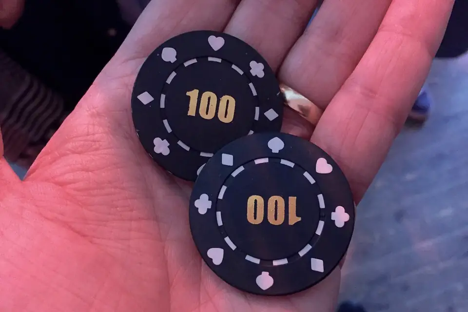 Hand holding two black casino chips marked 100